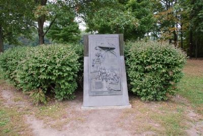 View of marker with bushes and grove of trees visible image. Click for full size.