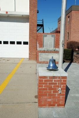 Memorial marker is behind the traditional firehouse bell image. Click for full size.