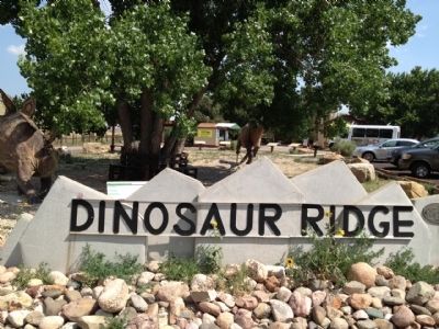 Dinosaur Ridge sign with dinosaurs and visitors center in background. image. Click for full size.