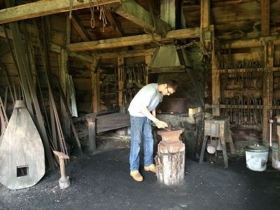 A National Park Service employee working in the blacksmith shop. image. Click for full size.