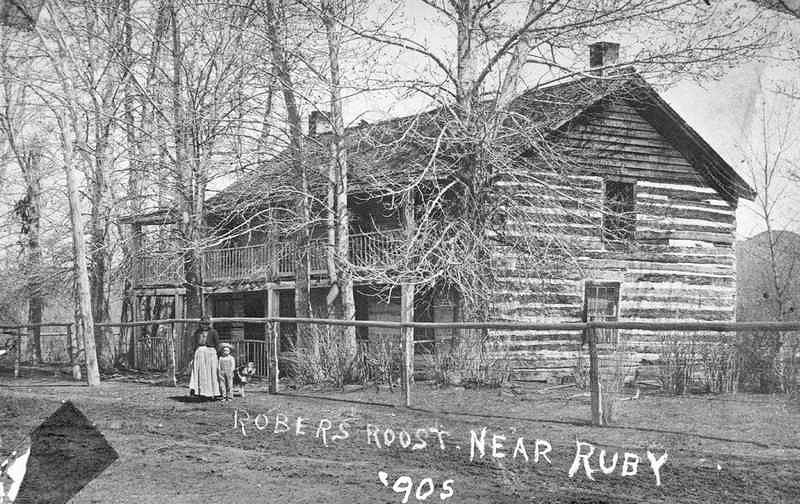 <i>Woman and Boy Stand in Front of the Robbers Roost a Two Story Log Cabin 1905</i> image. Click for full size.