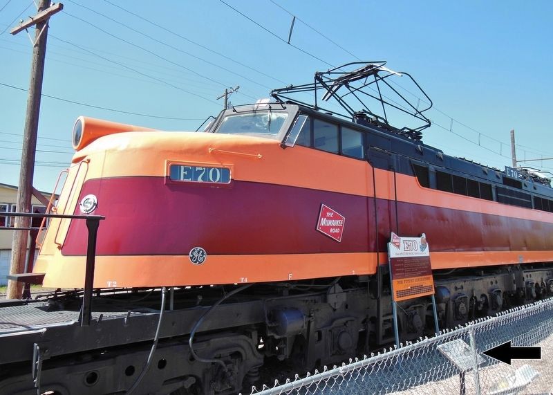 Electrified Railroad Marker (<i>wide view; marker visible inside fence, overlooking locomotive</i>) image. Click for full size.