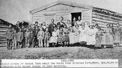 A group of school children and teacher posing in front of a log cabin in Adobetown, 1865 image. Click for full size.